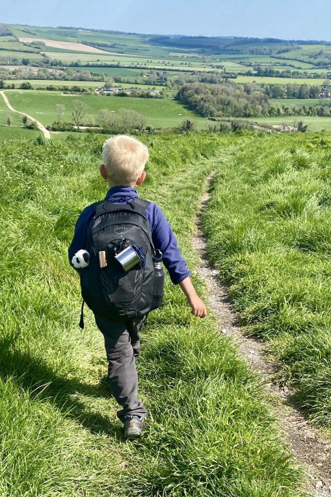 A young boy heads out on an adventure with backpack and teddy.
