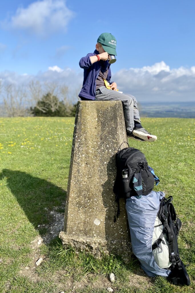 A young boy takes a drink break from hiking sitting atop a trig point.